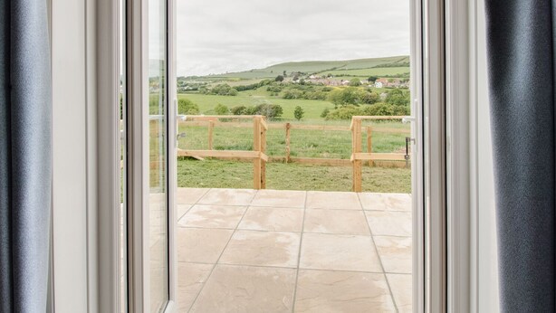 A view from a room with a glass door leading to a balcony with a wooden railing. - Village View (Bridport)