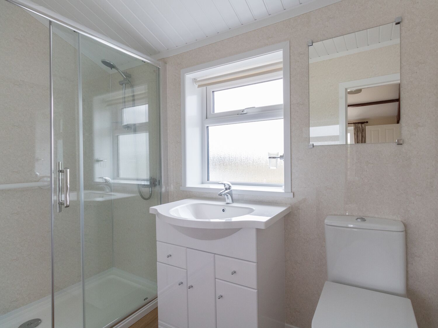 A bathroom with a glass shower enclosure, a white sink, and a toilet.