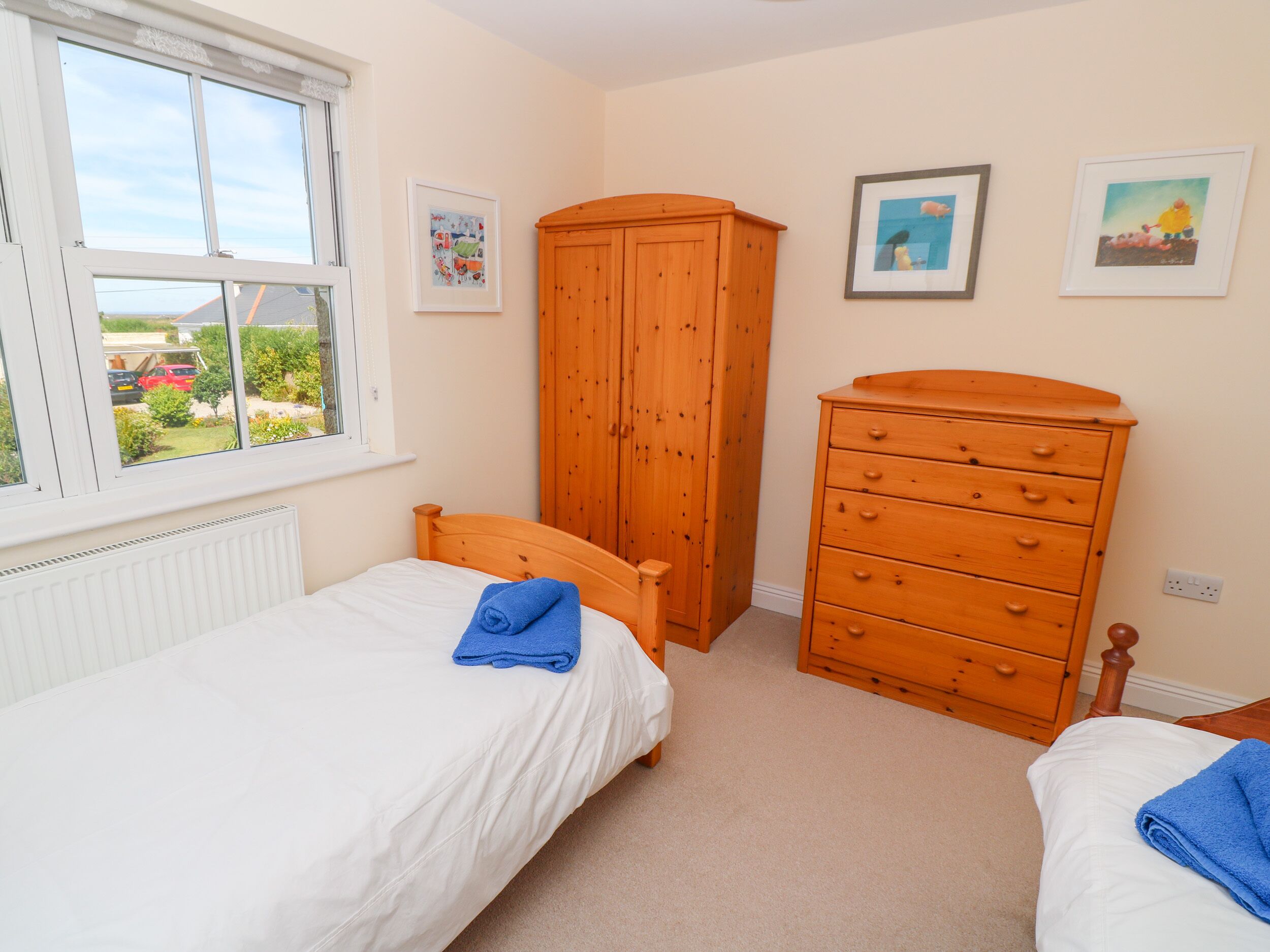 A bedroom with two beds, a wooden wardrobe, and a window with a view of the outside.