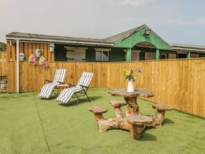 A wooden fence, two striped lounge chairs, a wooden table with benches, and a potted plant with flowers. - The Sequoia (Scarborough)