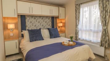 Une chambre à coucher bien rangée, avec un lit, des lampes de chevet, une fenêtre avec des rideaux et une petite table sur laquelle est posé un vase de fleurs.