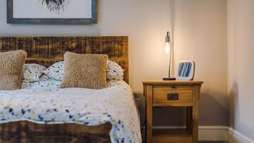 A neatly made bed with a patterned bedspread and two pillows, a wooden nightstand with a lamp and a framed picture, and a wall with a framed artwork.