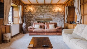 Una sala de estar acogedora con una pared de piedra, un sofá de cuero marrón, un sofá blanco y una mesa de centro de madera.