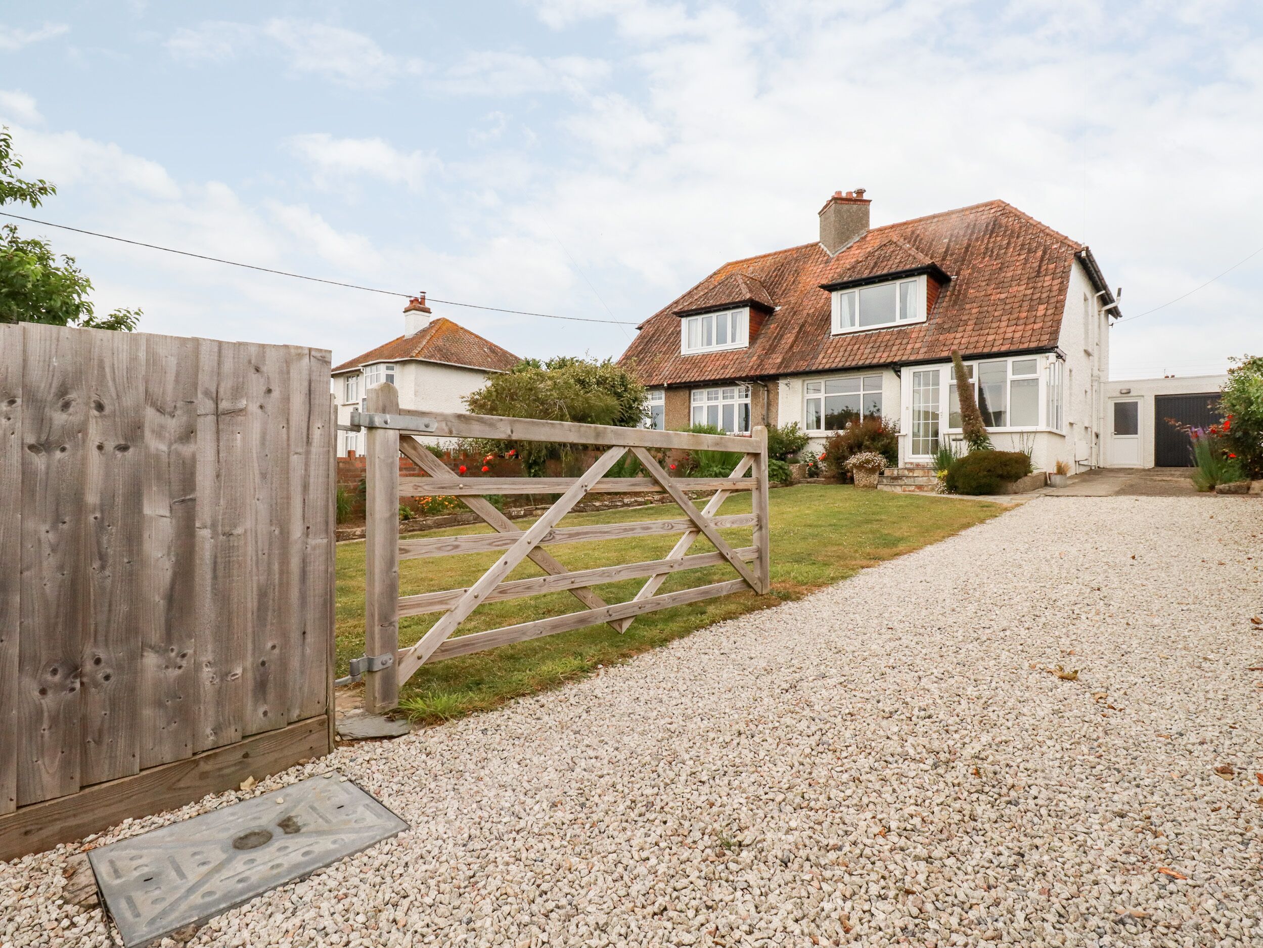 A residential property with a gravel driveway, a wooden gate, and a house with a tiled roof.