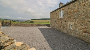 A stone building with a gravel courtyard, a stone wall, and a view of rolling hills. - The Aspens (Barnard Castle)