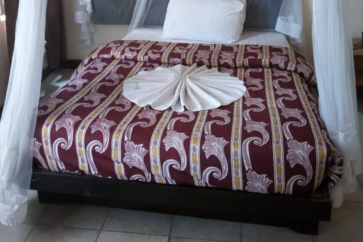 Een bed met hemel, een geborduurd beddegoed en een decoratief kussen.
