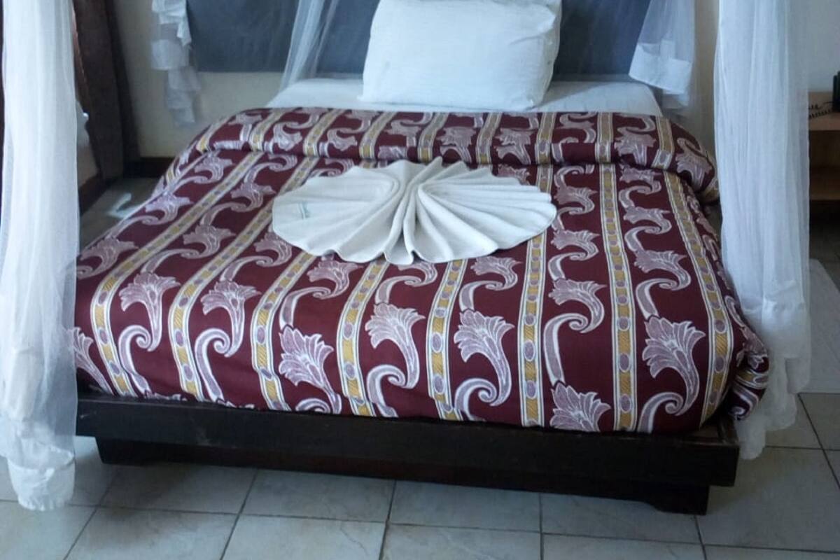 Een bed met hemel, een beddekleed met patroon en een decoratief kussen.