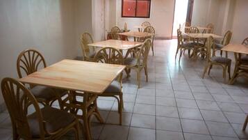 Comedor con varias mesas y sillas, piso de baldosas y ventana con contraventanas rojas.