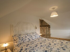 A bedroom with a bed, a wooden door, a white headboard, and a bedside lamp.