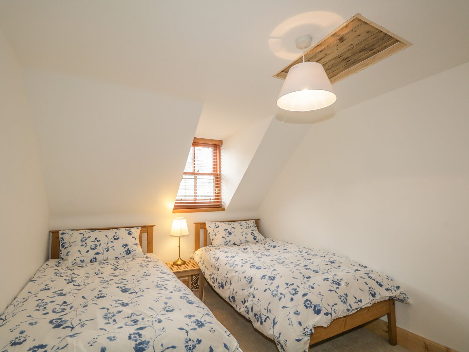 A small, cozy bedroom with two single beds, a skylight, a window, and a ceiling lamp.