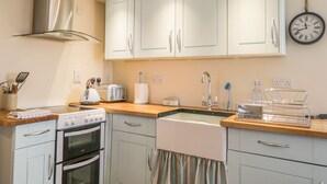 A kitchen with white cabinets, a stainless steel range hood, a double oven, a sink, and a clock on the wall. - 11 Village (Banff)