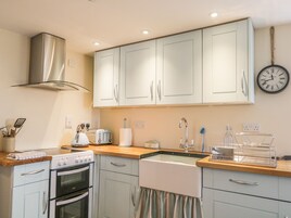 A kitchen with white cabinets, a stainless steel range hood, a double oven, a sink, and a clock on the wall.