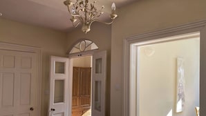 A hallway with white doors, a chandelier, and a wooden cabinet. - Sant Seiriol (Beaumaris)