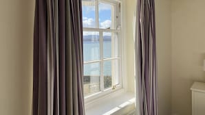 A room with a large window overlooking a body of water, a white radiator, and a small white cabinet. - Sant Seiriol (Beaumaris)