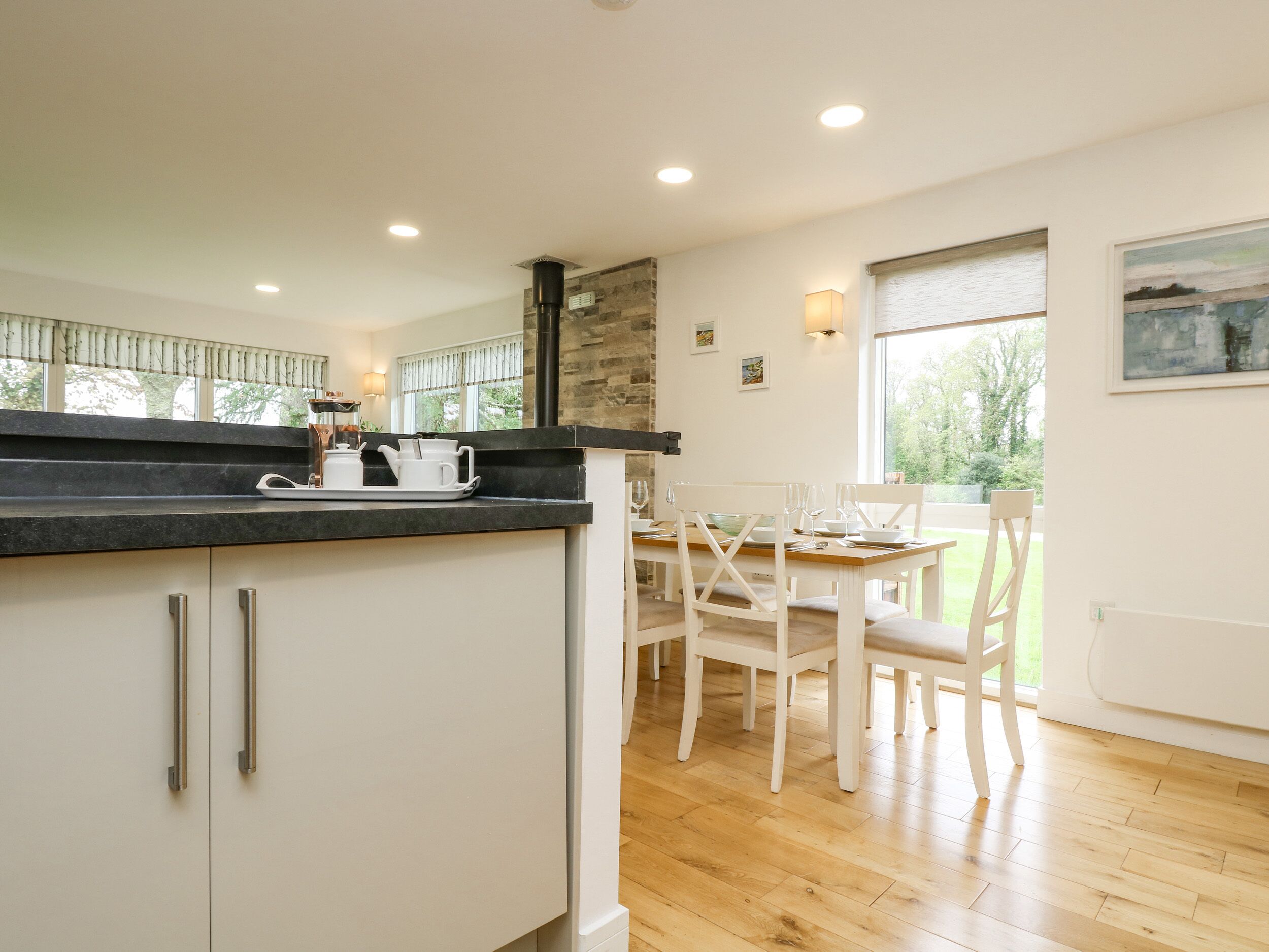 A modern kitchen with white cabinets, a black countertop, and a dining area with a wooden table and white chairs.