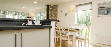 A modern kitchen with white cabinets, a black countertop, and a dining area with a wooden table and white chairs.