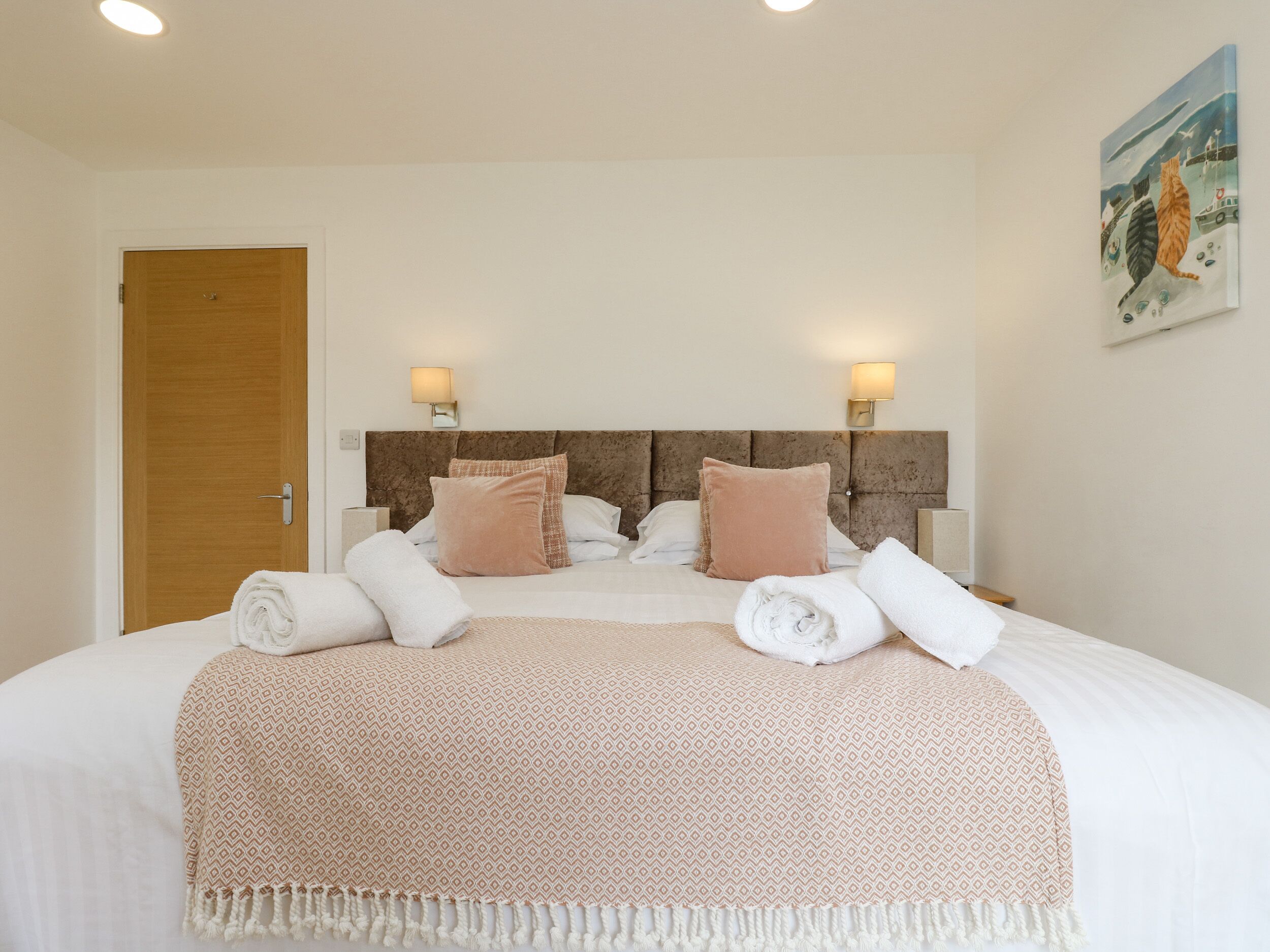 A neatly made bed with a patterned blanket, two wall-mounted lamps, and a painting on the wall.