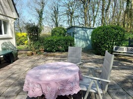 A patio with a table covered in a floral tablecloth, a metal chair, and a wooden bench.