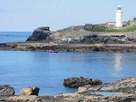 A coastal scene with a lighthouse, rocky shoreline, and calm sea.
