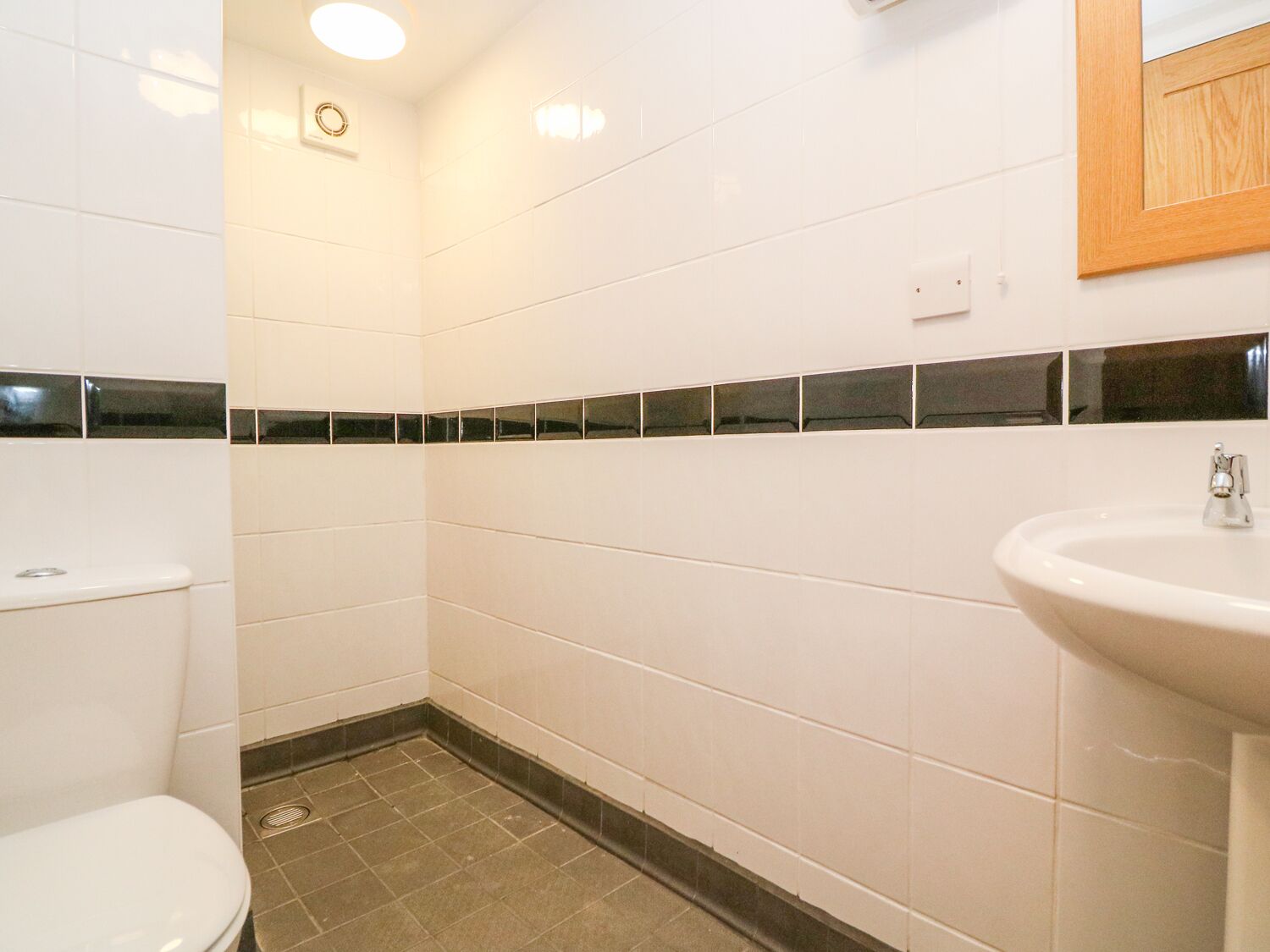 Un baño con azulejos blancos, un detalle de azulejos blanco y negro, un lavamanos y un inodoro.