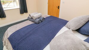 A neatly made bed with rolled towels, a wooden door, and a window with curtains. - The Old Cows House (Helston)
