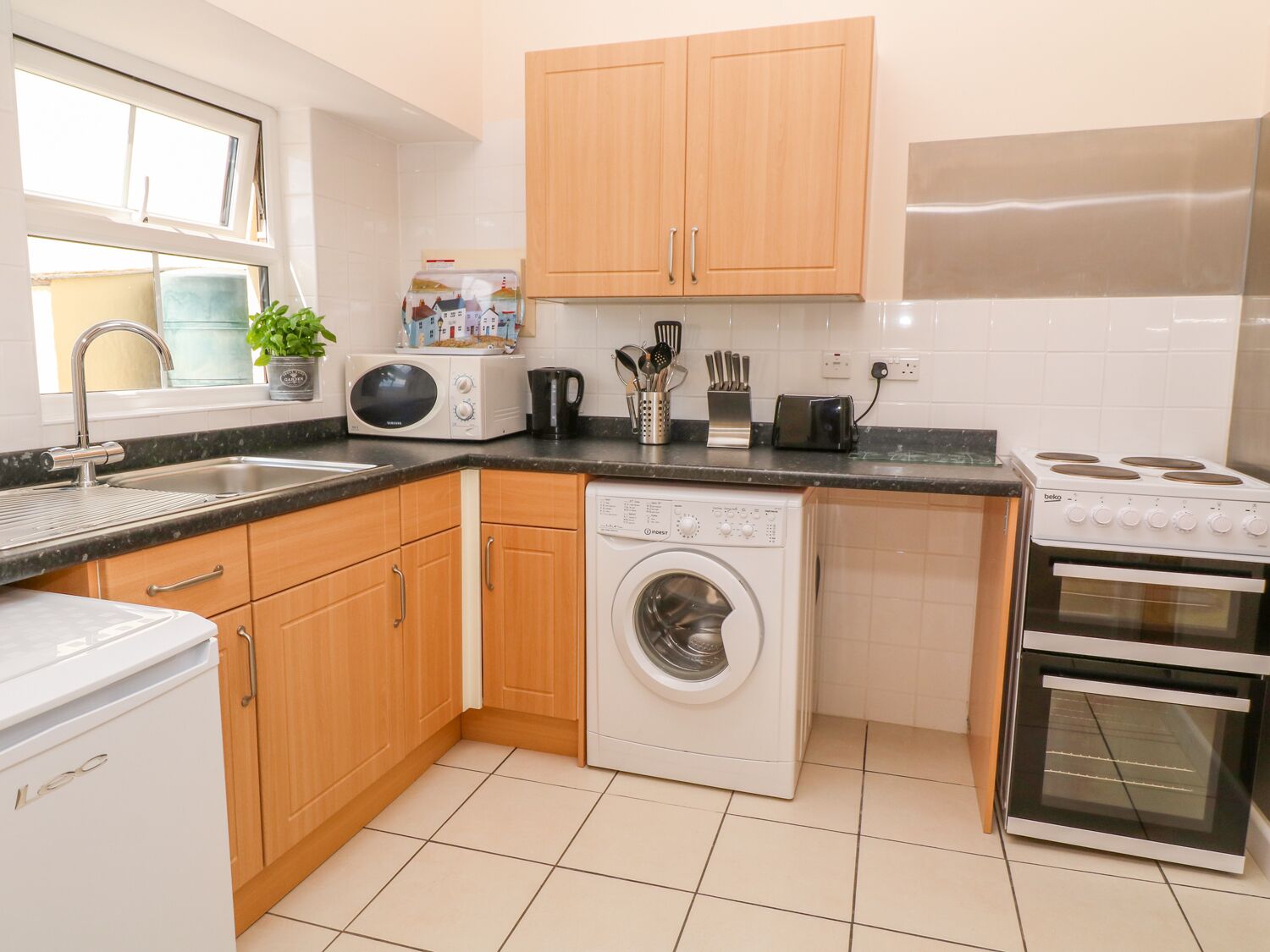 A compact kitchen with wooden cabinets, a washing machine, a microwave, a toaster, and a stove.