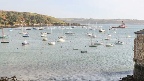 A harbor with numerous boats anchored in calm waters, a lighthouse in the distance, and a stone building on the right. - The Old Cows House (Helston)