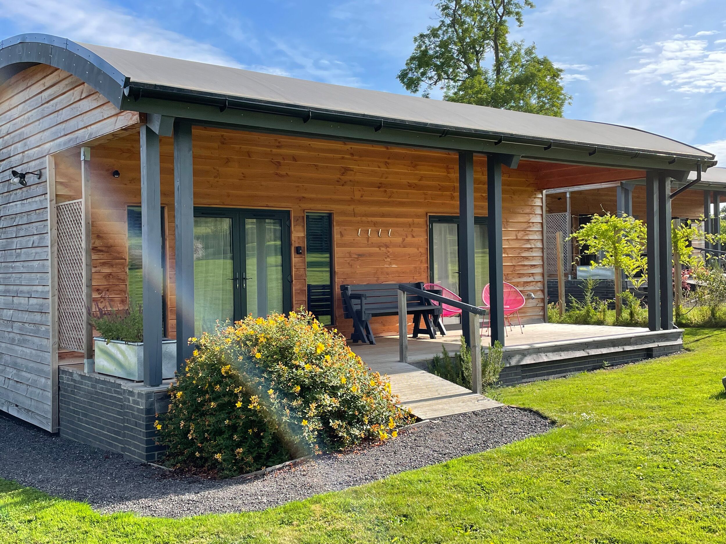 A modern wooden cabin with a covered porch, a dining area with outdoor furniture, and a small garden.