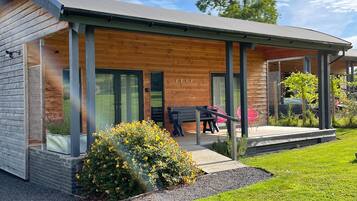 A modern wooden cabin with a covered porch, a dining area with outdoor furniture, and a small garden.