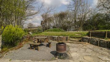 A rustic outdoor seating area with a wooden table and benches, surrounded by stone walls and greenery.