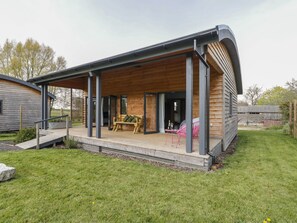 A modern house with a covered porch, a wooden deck, and a small garden area. - Bluebell (Shepton Mallet)