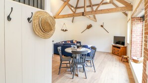 A cozy room with a dining area, a blue sofa, and a television. - The Granary (Dereham)