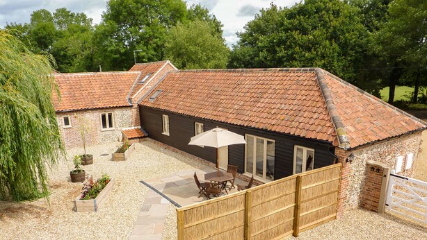A rustic house with a tiled roof, a patio with a table and chairs, and a wooden fence. - The Granary (Dereham)