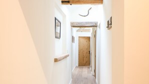 A narrow hallway with wooden beams, a wooden door, and a small shelf with a picture frame. - The Stables (Dereham)