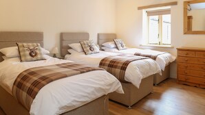 A bedroom with two beds, a dresser, and a window with a view. - The Stables (Dereham)