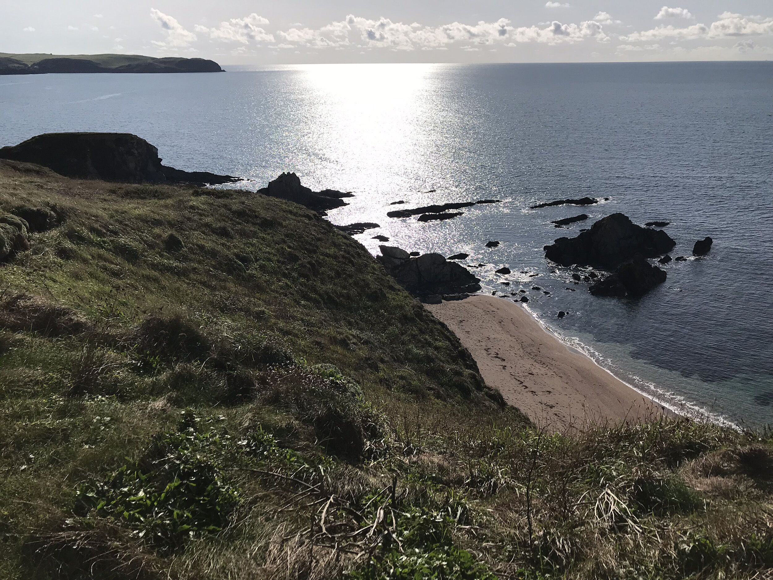 A coastal landscape with a beach, rocky outcrops, and a distant landmass.