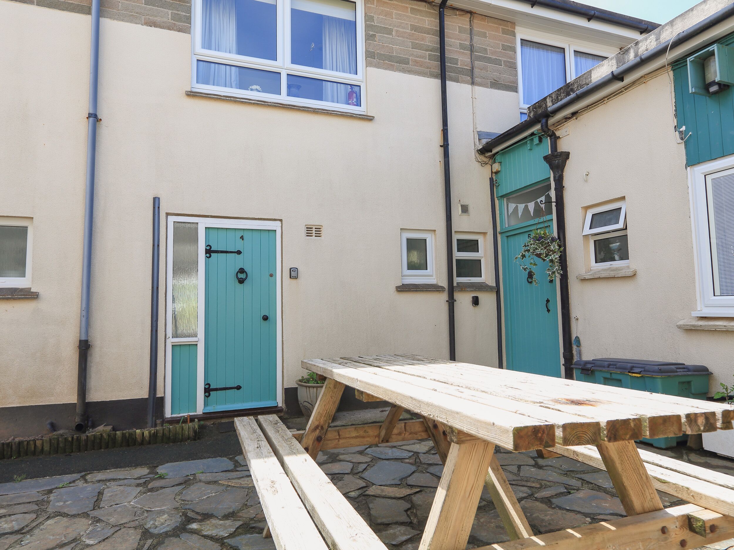 A courtyard with a wooden bench, a turquoise door, and a small window.