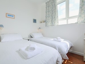 A hotel room with two beds, a window with floral curtains, a bedside table with a lamp, and a wall-mounted thermostat. - 4 Thornlea Mews (Kingsbridge)