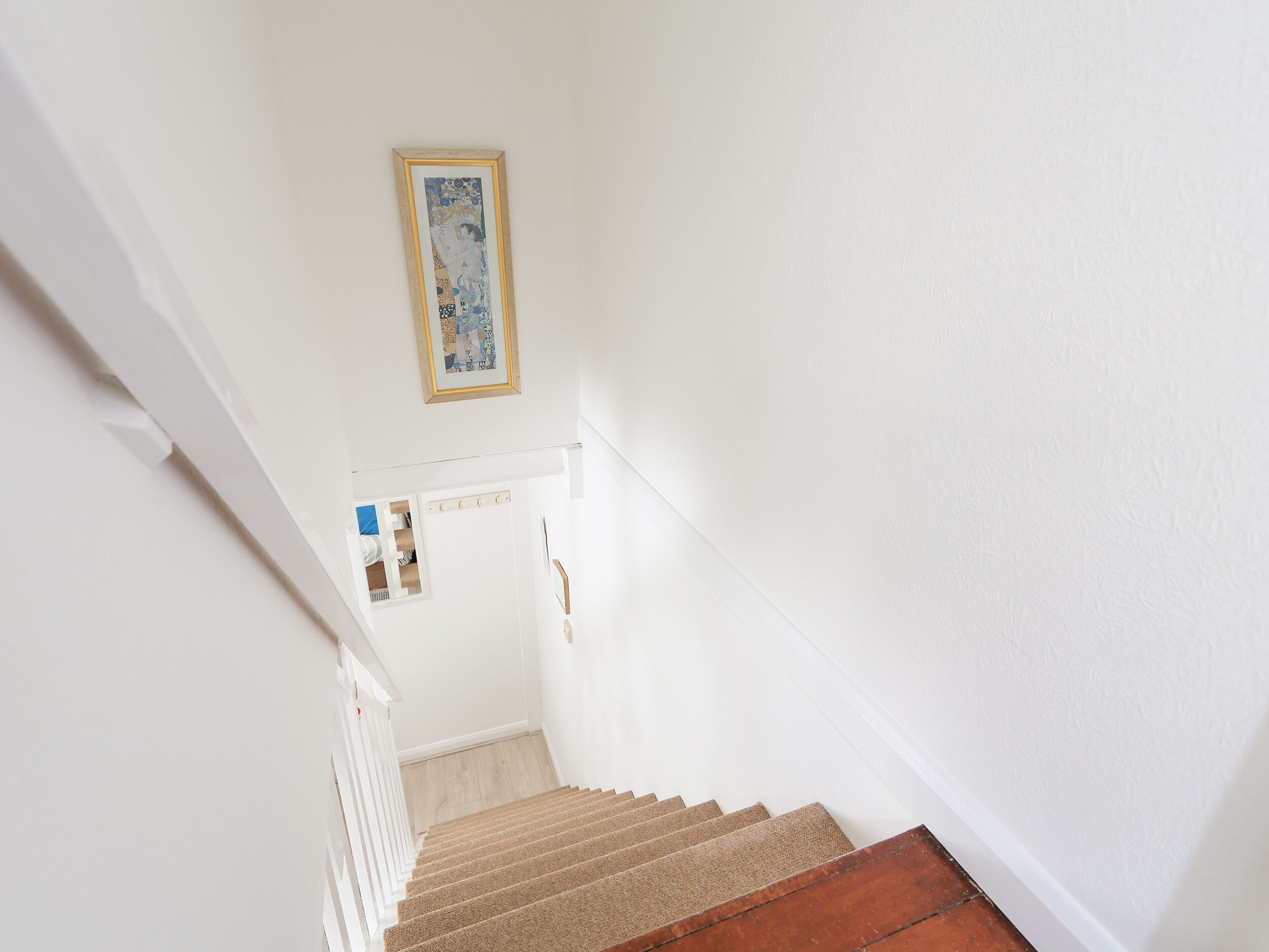 A staircase with a wooden handrail and carpeted steps leading to a landing with a white door and a framed picture above it.