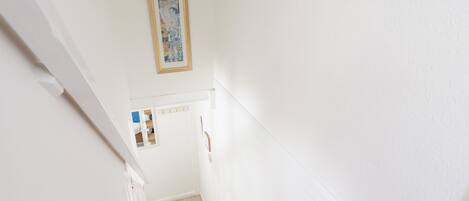 A staircase with a wooden handrail and carpeted steps leading to a landing with a white door and a framed picture above it.