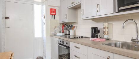 A modern kitchen with white cabinets, stainless steel appliances, and a visible fire blanket.
