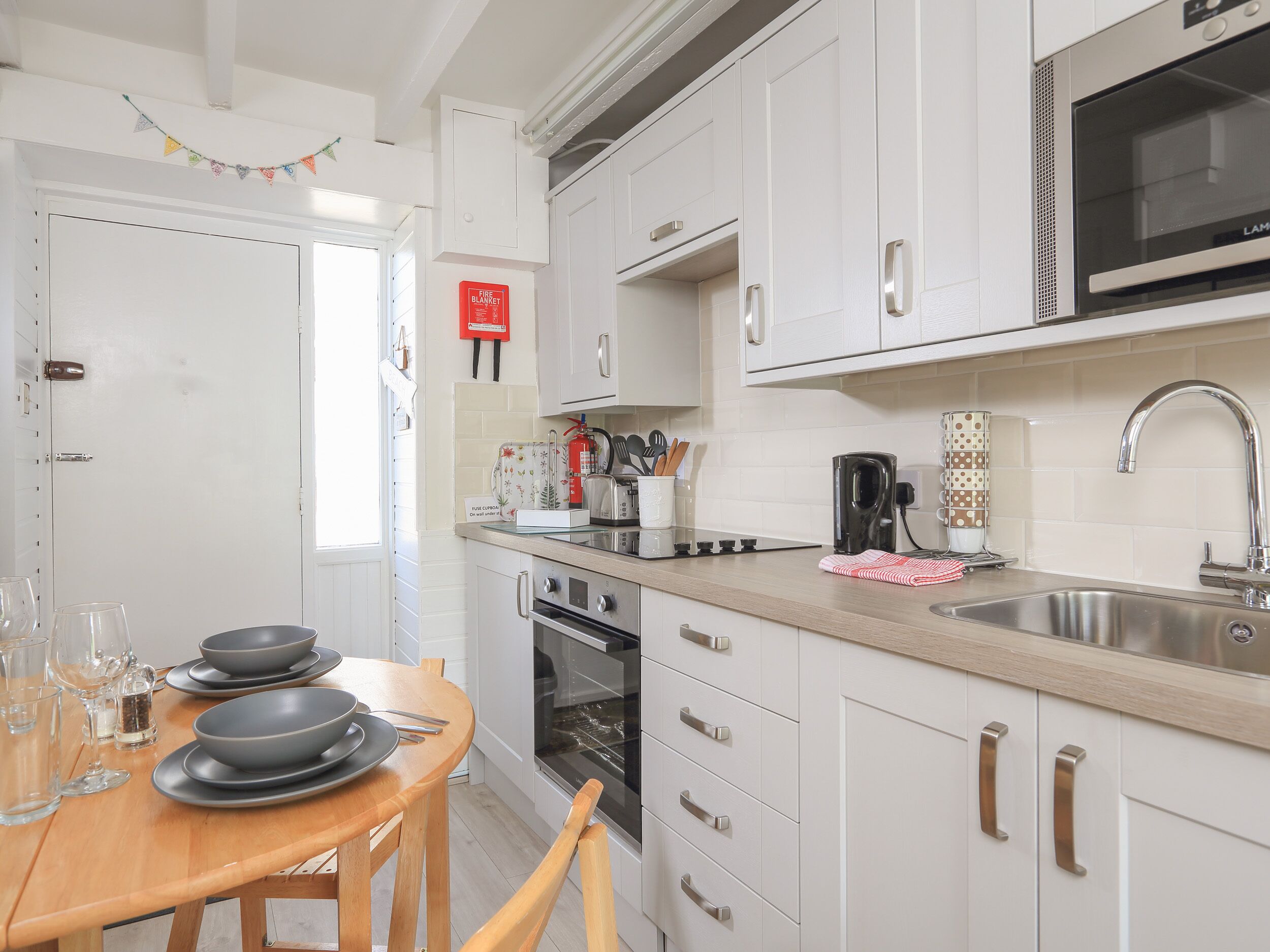 A modern kitchen with white cabinets, stainless steel appliances, and a wooden dining table set for four.