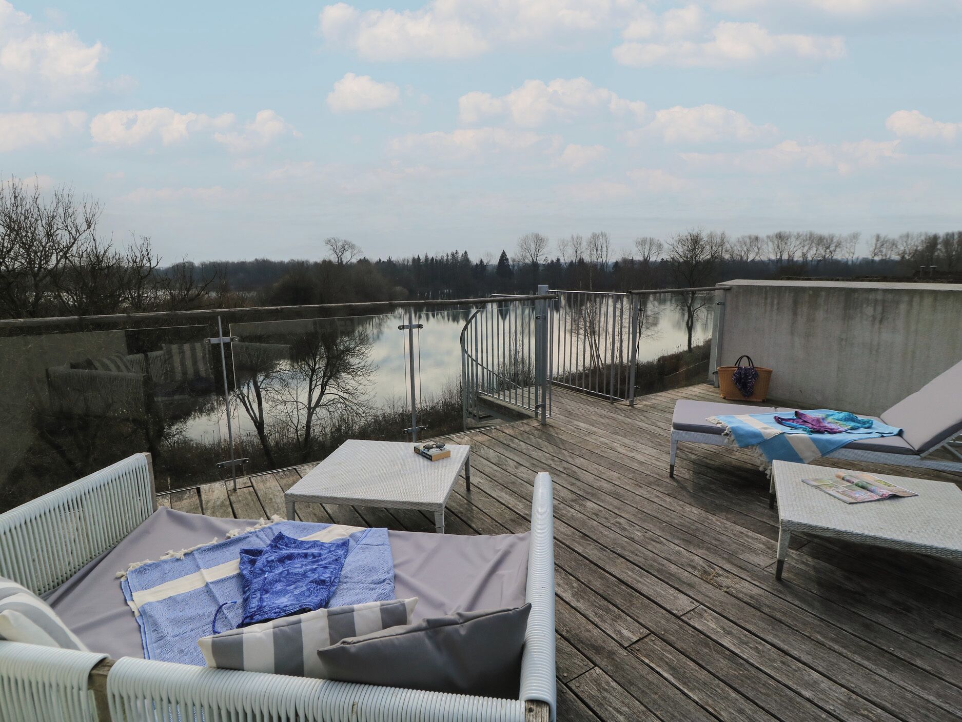 Une terrasse en bois avec deux chaises longues et une table, donnant sur une étendue d’eau calme et des arbres.