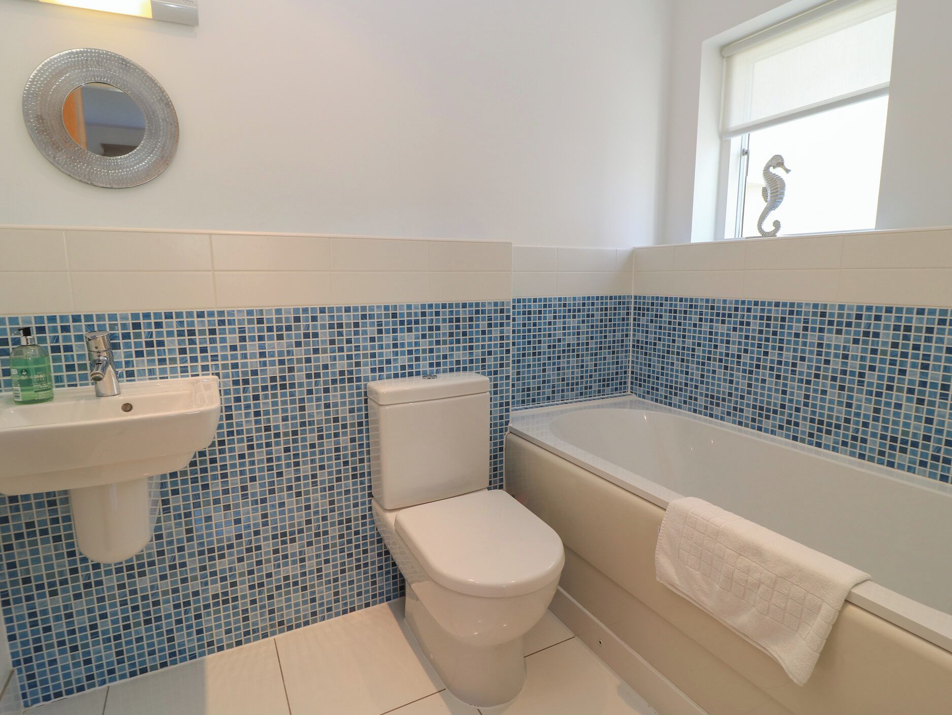 A bathroom with a toilet, sink, and bathtub, featuring blue mosaic tiles on the walls.