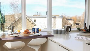 Eine moderne Küche mit großem Fenster, Frühstücksangebot mit Croissants, Saft und Kaffee, sowie einer Obstschale.