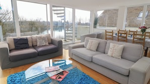 Ein modernes Wohnzimmer mit zwei Sofas, einem Glastisch und Seeblick durch große Fenster.
