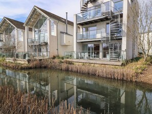 En moderne boligbygning med et spejlende vandbassin foran, med altaner med glasgelændere og en trappe.