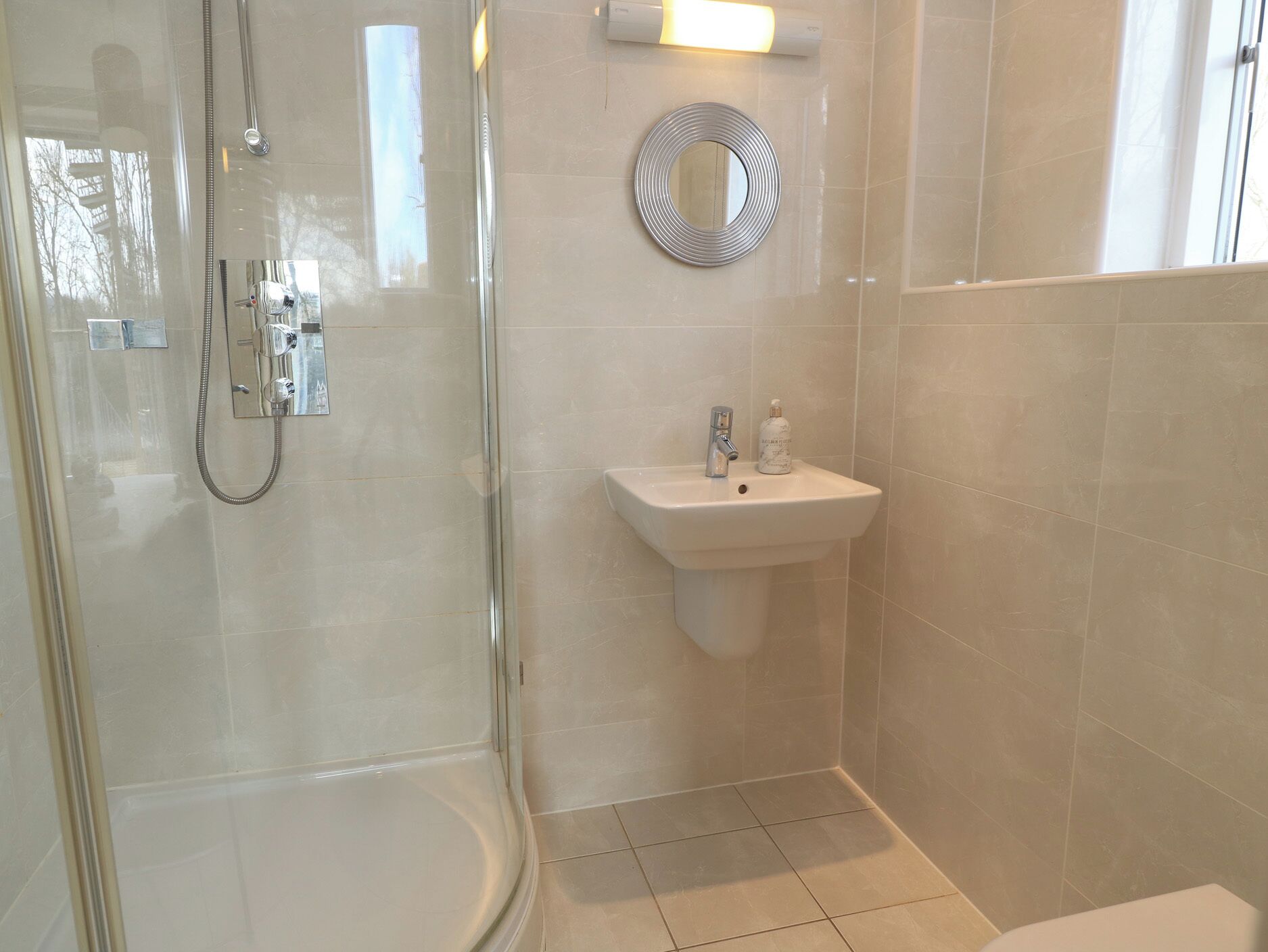 Un bany modern amb dutxa de vidre, un lavabo amb pedestal i un mirall.