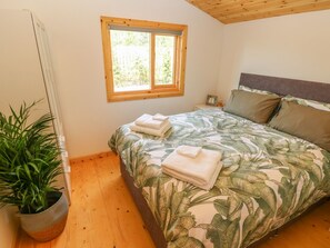 Un dormitorio con cama, ventana, mesita de noche, planta en maceta y techo de madera.