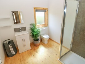 A bathroom with a wooden floor, a white sink, a toilet, a window, a shower, and a plant. - Willow Lodge (Tenby)